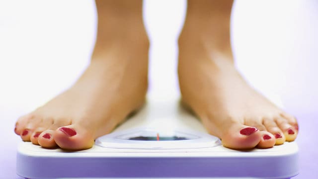 A woman checking her weight on a bathroom scale.